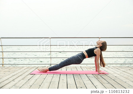 Young girl on yoga mat on wooden floor outdoors 110813232