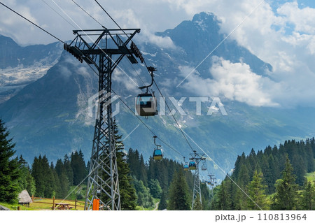 Cable car in Swiss Alps. Gondola from Grindelwald in Jungfrau. Summer Alpine landscape with snowcapped mountains background. Transport tourists uphill 110813964