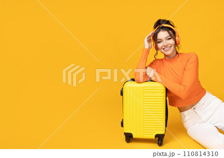 A young girl in headphones and with a yellow suitcase A young girl in headphones and with a yellow suitcase 110814310