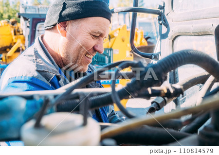 Mechanic repairs engine of tractor or heavy equipment. Farmer inspects and diagnoses agricultural Mechanic repairs engine of tractor or heavy equipment. Farmer inspects and diagnoses agricultural 110814579