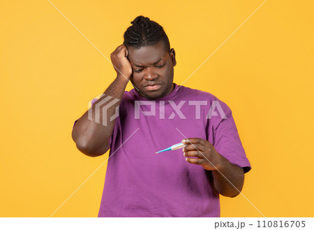 Sick black guy measuring temperature looking at thermometer, yellow background Sick black guy measuring temperature looking at thermometer, yellow background 110816705