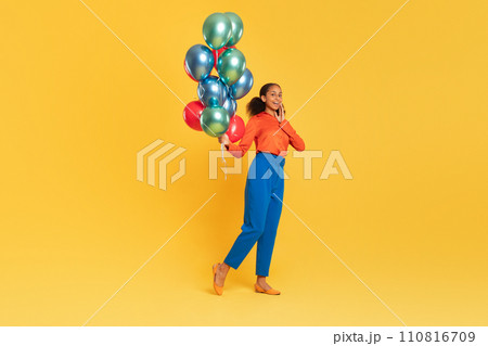 African teen girl with bunch of balloons on yellow backdrop African teen girl with bunch of balloons on yellow backdrop 110816709