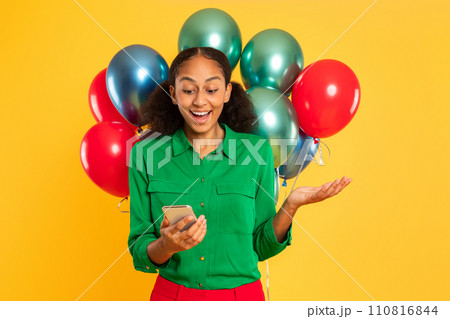 Excited African teenager girl texting on phone with balloons, studio Excited African teenager girl texting on phone with balloons, studio 110816844