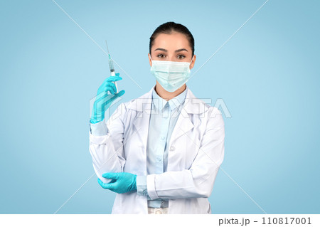 European lady doctor in white coat and surgical mask holding syringe, preparing for vaccination or medical procedure 110817001