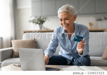 senior lady smiling shopping on laptop holding credit card indoor 110817223