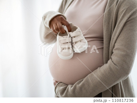 Cropped of pregnant woman holding small baby shoes, window background 110817236