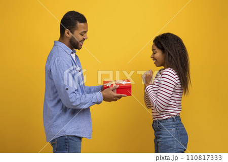 Happy young black man giving red gift box to his delighted girlfriend 110817333