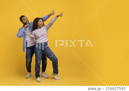 Check This. Happy black couple pointing at copy space on yellow background 110817585