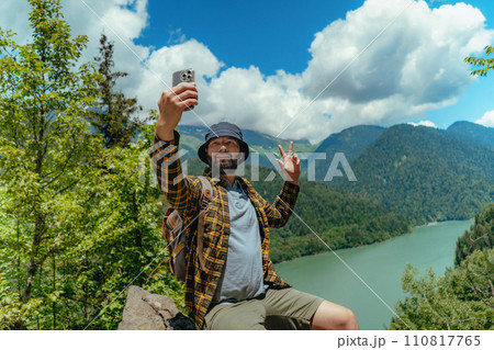 Hiking traveller handsome caucasian bearded man with backpack taking selfie against view of Lake Ritsa in Abkhazia Hiking traveller handsome caucasian bearded man with backpack taking selfie against view of Lake Ritsa in Abkhazia 110817765