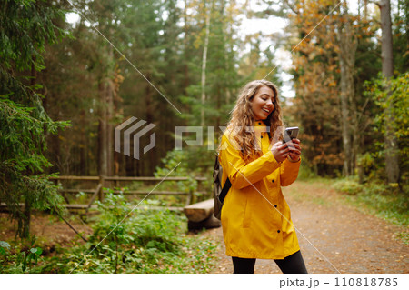 Travel apps. Curly young woman traveler in yellow coat holding smartphone in hand. Concept of travel 110818785