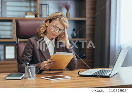 A professional senior woman engrossed in work at her home office, embodying dedication and remote business management. 110819024