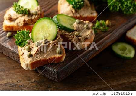 Open sandwiches with pate, cucumber, capers, and parsley on a old cutting board. Open sandwiches with pate, cucumber, capers, and parsley on a old cutting board. 110819158