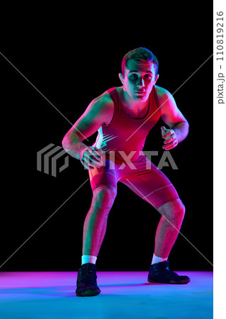 Young man, professional freestyle fighter stands in attacking pose and looking at camera against black background in mixed neon lights. 110819216