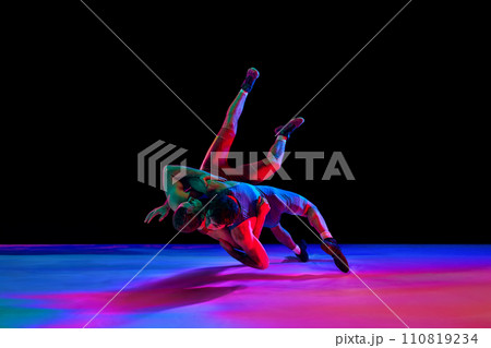 Greco-Roman, freestyle wrestling. Two sportsman, fighting in red and blue uniform in action against black background in mixed neon lights. 110819234