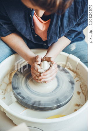 A woman ceramist at a pottery wheel in a workshop. The beginning of shaping a white clay product on a potter's wheel 110820679