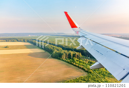 View of airplane wing, blue skies and green land during landing. Airplane window view. 110821201