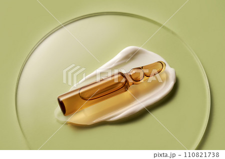 Ampoule in a drop of cosmetic cream on a green background. 110821738