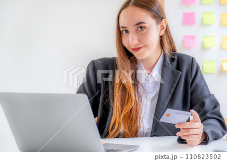 Caucasian businesswoman hand hold mock-up credit card for online shopping on smartphone or laptop computers from home office, payment e-commerce, internet finance bank, spend money electronic wallet 110823502