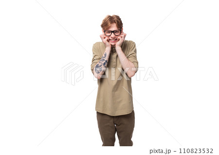 handsome young red-haired man in a beige shirt wears eyeglasses on a white background 110823532