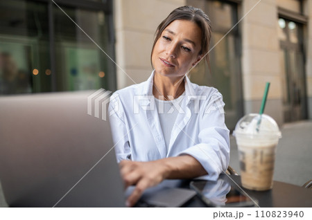 Contented cute woman sitting at the table in a street cafe 110823940