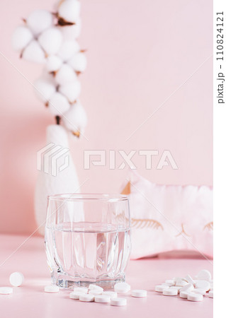 Sleeping pills, a glass of water and a sleep mask on a pink background  vertical view 110824121