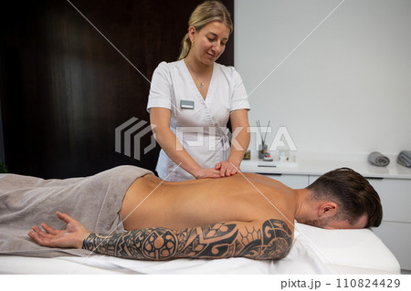Young man with a big tattoo having back massage session in a salon Young man with a big tattoo having back massage session in a salon 110824429