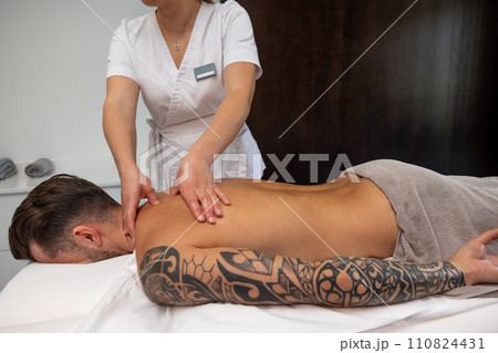 Young man with a big tattoo having back massage session in a salon Young man with a big tattoo having back massage session in a salon 110824431