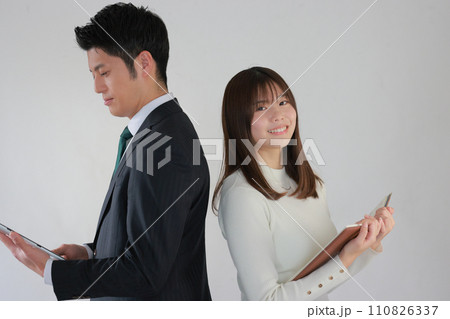 背中合わせ_タブレットを見て考えるビジネスマンと本を開くビジネスウーマン_1 110826337