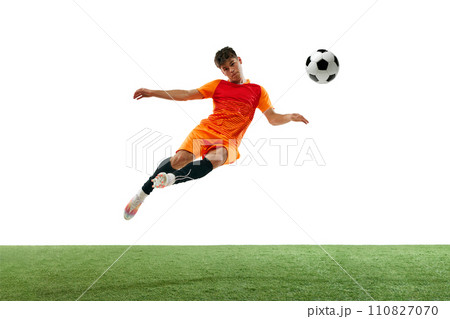 Dynamic image of competitive young man in orange uniform training, hitting ball in a jump isolated over white background with grass flooring 110827070
