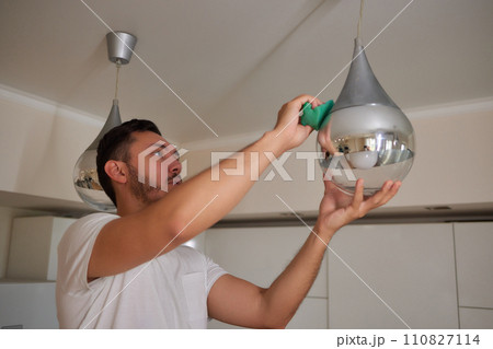 Extreme close-up of unrecognizable man cleaning electric lamp with wet microfiber rag. Close-up of male hands wiping chandelier removing dust at home. Concept of cleaning and household, slow motion. Extreme close-up of unrecognizable man cleaning electric lamp with wet microfiber rag. Close-up of male hands wiping chandelier removing dust at home. Concept of cleaning and household, slow motion. 110827114