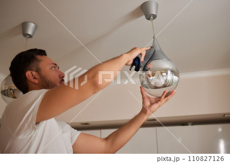 Extreme close-up of unrecognizable man cleaning electric lamp with wet microfiber rag. Close-up of male hands wiping chandelier removing dust at home. Concept of cleaning and household, slow motion. 110827126