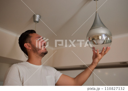 Extreme close-up of unrecognizable man cleaning electric lamp with wet microfiber rag. Close-up of male hands wiping chandelier removing dust at home. Concept of cleaning and household, slow motion. 110827132