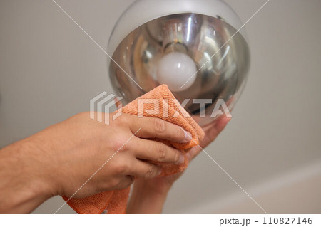 Extreme close-up of unrecognizable man cleaning electric lamp with wet microfiber rag. Close-up of male hands wiping chandelier removing dust at home. Concept of cleaning and household, slow motion. Extreme close-up of unrecognizable man cleaning electric lamp with wet microfiber rag. Close-up of male hands wiping chandelier removing dust at home. Concept of cleaning and household, slow motion. 110827146