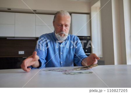 Portrait of bearded senior pensioner male with wrinkled hands counting Russian ruble banknotes sitting at home table. Portrait of bearded senior pensioner male with wrinkled hands counting Russian ruble banknotes sitting at home table. 110827205