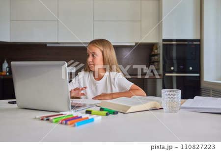 Thirsty little schoolgirl writing in exercise book, taking break and drinking fresh cool filtered clear aqua, preventing dehydration, sitting at table by window. Preteen girl using laptop for homework Thirsty little schoolgirl writing in exercise book, taking break and drinking fresh cool filtered clear aqua, preventing dehydration, sitting at table by window. Preteen girl using laptop for homework 110827223