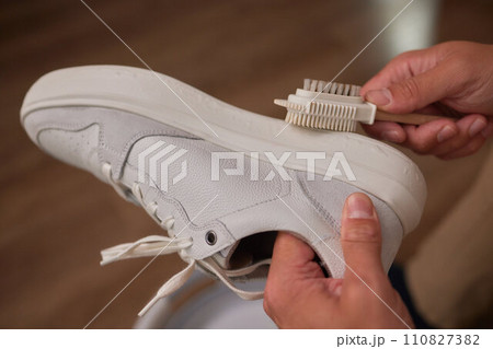 Cleaning suede sneakers. A worker in a shoe workshop cleans a pile of shoes Cleaning suede sneakers. A worker in a shoe workshop cleans a pile of shoes 110827382