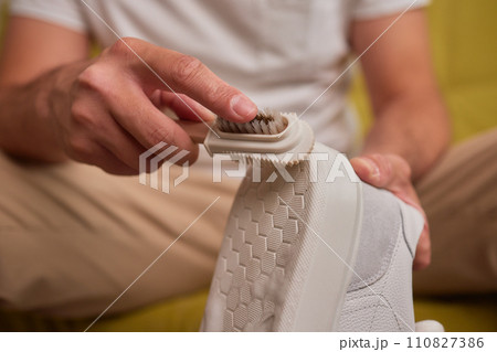 Cleaning suede sneakers. A worker in a shoe workshop cleans a pile of shoes Cleaning suede sneakers. A worker in a shoe workshop cleans a pile of shoes 110827386