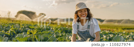 Smiling female farmer in uniform working in cabbage field during harvest. Agricultural activity 110827974