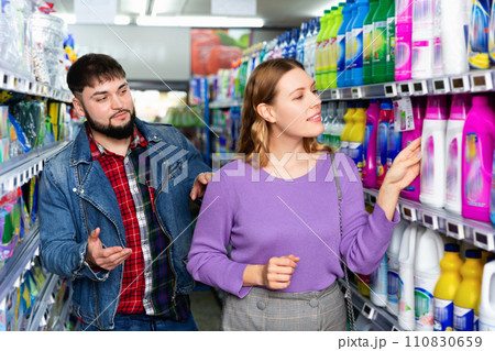 Portrait of positive young woman and man choosing liquid laundry detergents during shopping at supermarket 110830659
