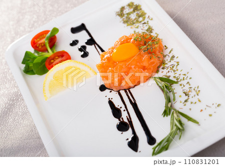 Fresh tartar with salmon, balsamic, greens and lemon on white plate 110831201