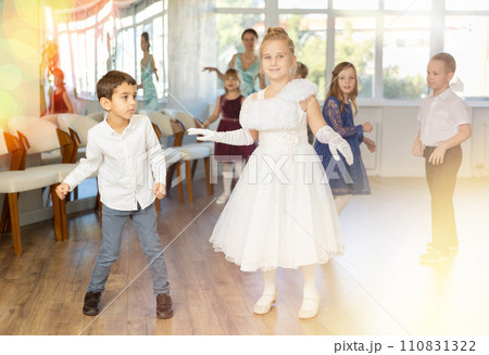 Little children in elegant dresses practicing twist dance in school hall 110831322
