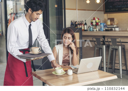 Restaurant business Handsome waiter serving food to young beautiful women with smiling face. Businesswoman using computer laptop while working on luch time. Waiter Man serving coffee cup in cafe 110832144