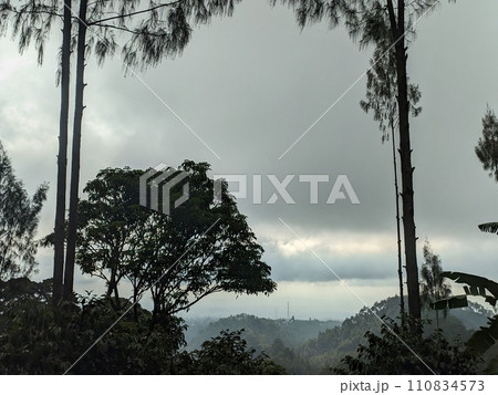 The road is in the middle of forests and mountains which are cloudy and cool 110834573