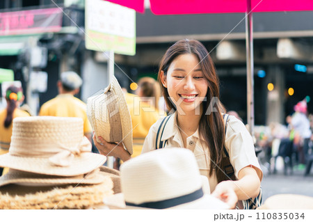 Young Asian woman traveler tourist shopping for a hat and walking at outdoor market in Bangkok in Thailand. People traveling, summer vacation and tourism 110835034