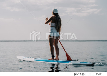 Woman sea sup. Close up portrait of happy young caucasian woman with long hair looking at camera and smiling. Cute woman portrait in bikini posing on sup board in the sea 110835055