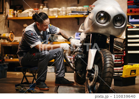 Mechanic in uniform repairing motorcycle of client 110839640
