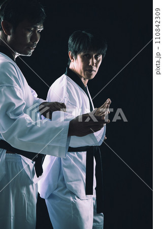 Two Men in Traditional Dobok Execute TaeKwonDo Techniques in High Contrast Setting 110842309