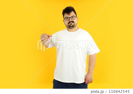 A man with a blank white t-shirt, on a yellow background. 110842545