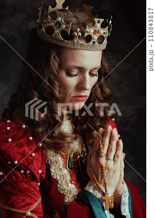 medieval queen in red dress with rosary and crown praying medieval queen in red dress with rosary and crown praying 110843817