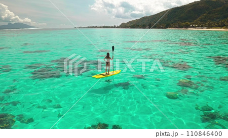 Woman standing on yellow sup board with paddle. Crystal turquoise water coral reef, tropical island. Active water sport during summer holidays. Concept of tourism and travel. Polynesia 110846400